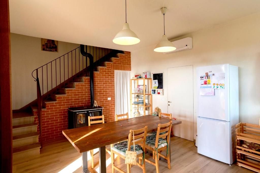 Una cocina con una mesa y sillas de madera, un refrigerador blanco y una pared de ladrillo con una escalera.