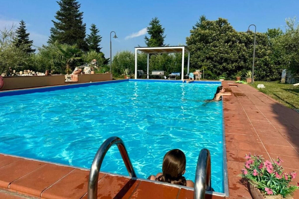 Una piscina con superficie de agua azul cristalina, rodeada por un jardín con diversas plantas y árboles.