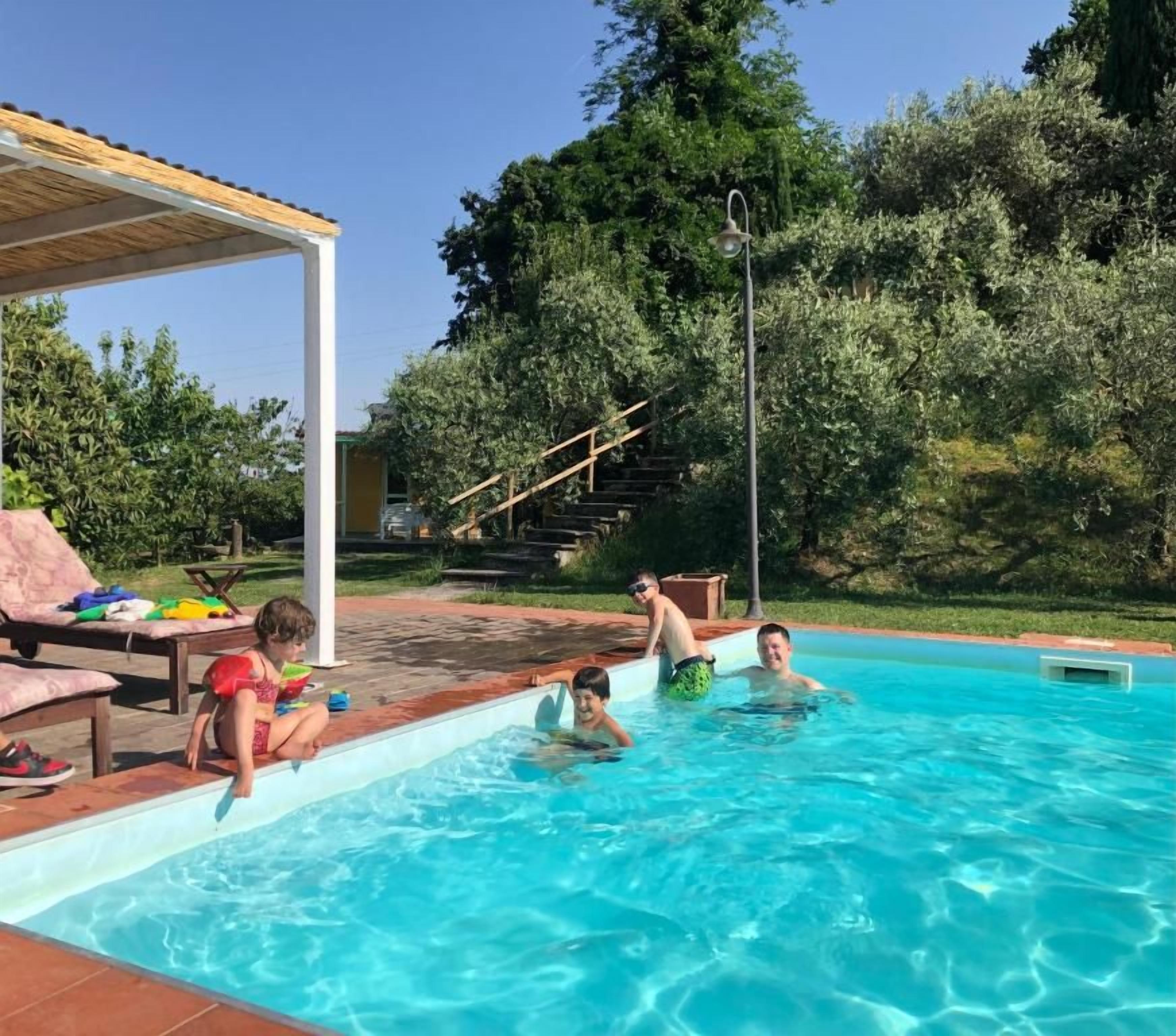 Una piscina con gente a su alrededor, un área de descanso cubierta y una escalera que conduce a un nivel superior.