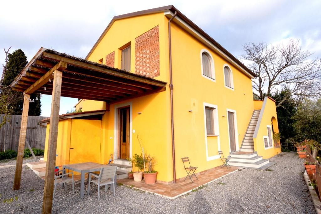 Una casa amarilla con un porche cubierto, una escalera y un camino de entrada de grava.