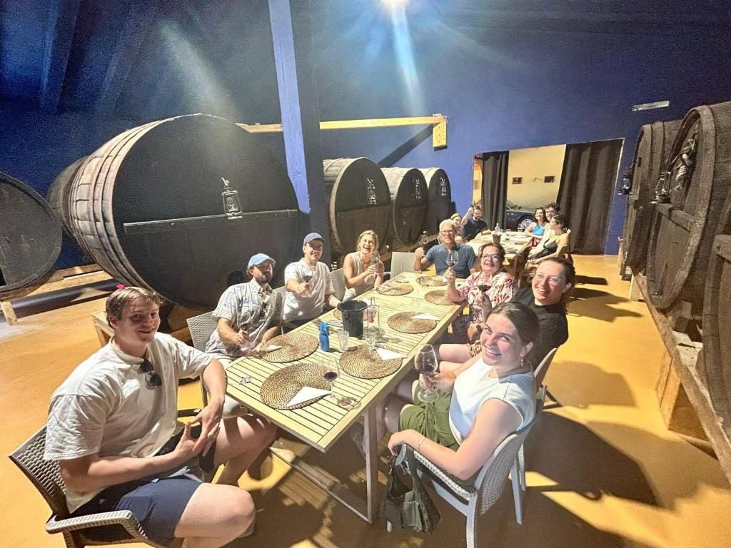 A group of people seated around a table in a room with barrels and a blue wall.