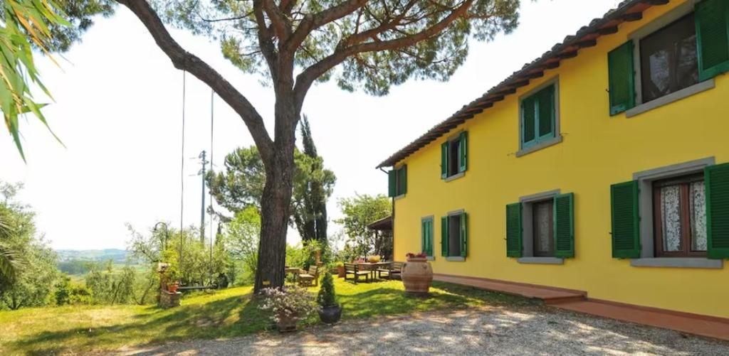 Un edificio giallo con persiane verdi, immerso nel verde sotto un cielo sereno.
