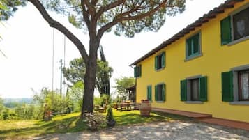Un edificio giallo con persiane verdi, immerso nel verde sotto un cielo sereno.