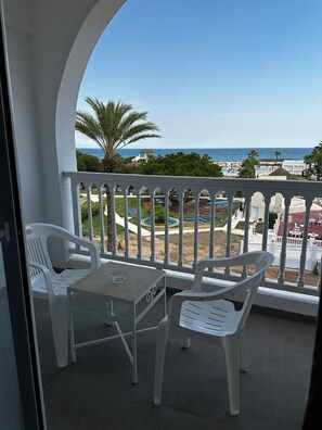 A balcony with a table and chairs, overlooking a pool area with palm trees and a view of the sea. - Tanfous Beach & Aquapark (Hammamet)