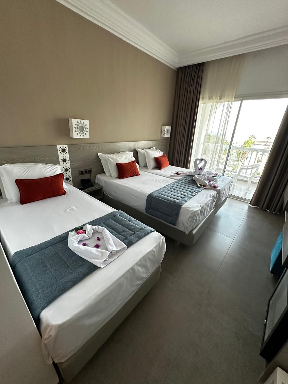 A hotel room with two beds, a large window, and a balcony.
