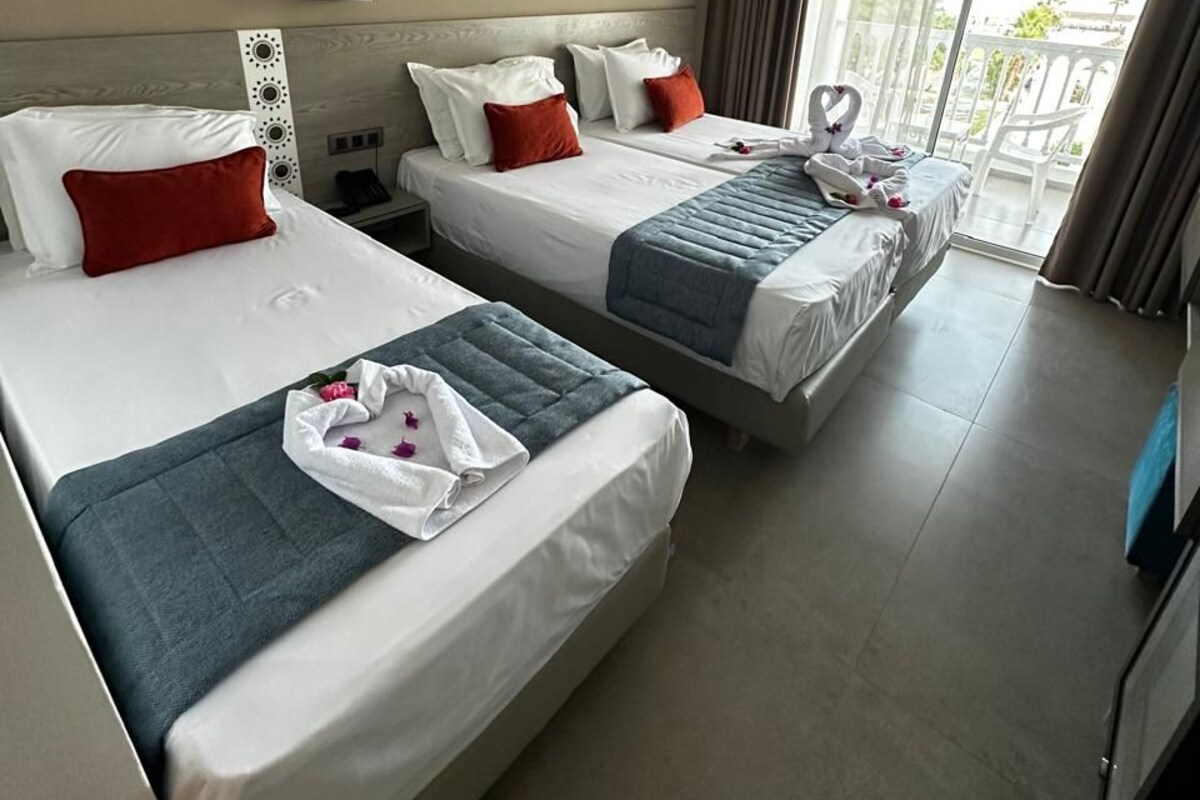 A hotel room with two beds, a large window, and a balcony.