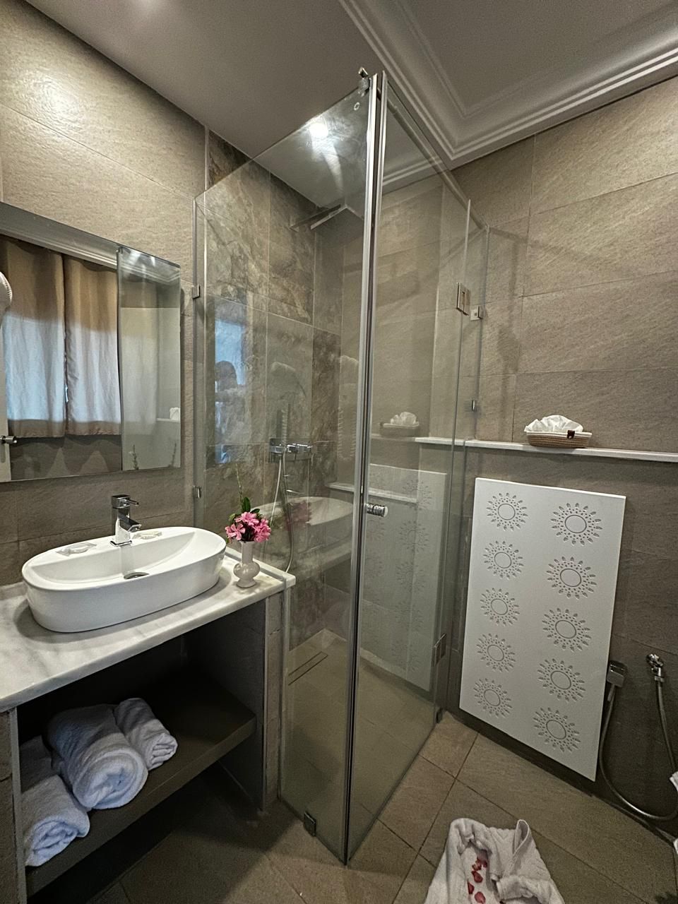 A modern bathroom with a glass-enclosed shower, a white sink, and a towel shelf.