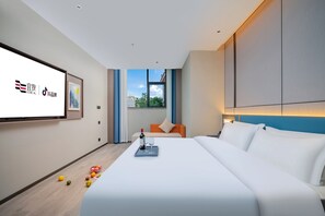 A modern hotel room with a large bed, a TV screen, and a window with a city view.