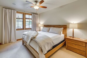 Ein Schlafzimmer mit einem Bett, zwei Nachttischen, einem Deckenventilator und einem Fenster mit Vorhängen.