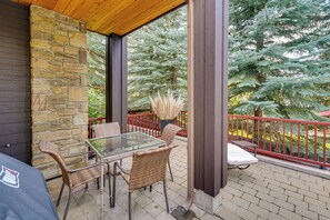 A covered patio area with a stone wall, a glass table, wicker chairs, and a red railing. - Sun Valley Extended Stay: Central Condo w/ Patio (Ketchum)