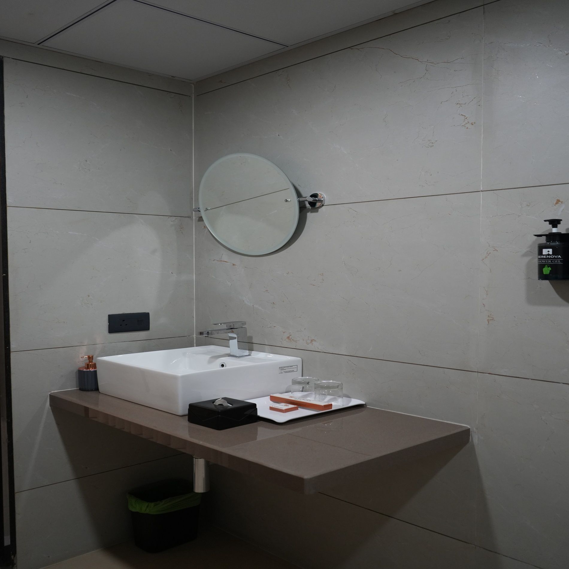 Un baño moderno con un lavabo rectangular, un espejo redondo y un dispensador de jabón.