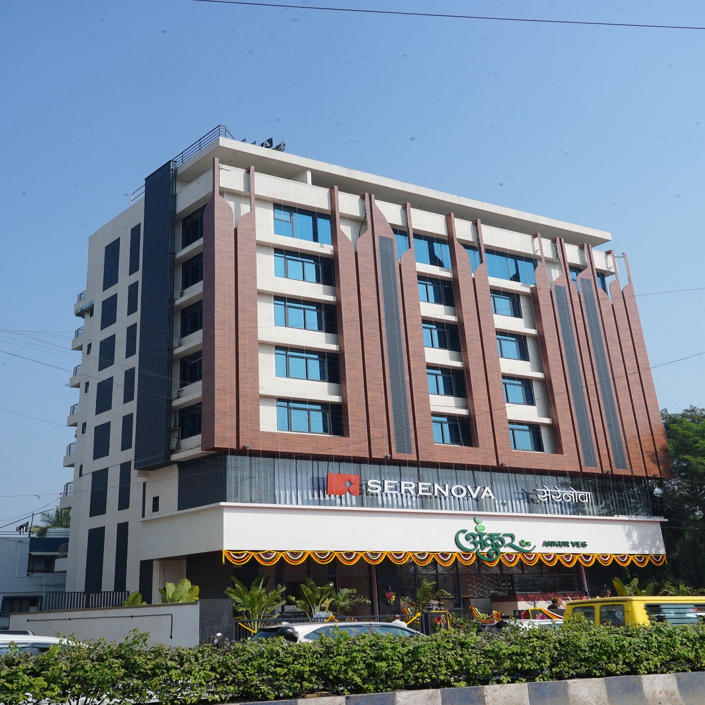Un hotel de varios pisos con un diseño moderno, que destaca un letrero de 'SERENOVA' y un restaurante llamado 'Ankur Veg' en la planta baja.