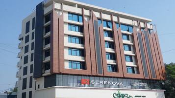 Un hotel de varios pisos con un diseño moderno, que destaca un letrero de 'SERENOVA' y un restaurante llamado 'Ankur Veg' en la planta baja.