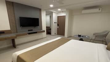 Habitación de hotel con una cama grande, un televisor de pantalla plana en la pared, un escritorio con una silla, una mesita pequeña y un ventilador de techo.