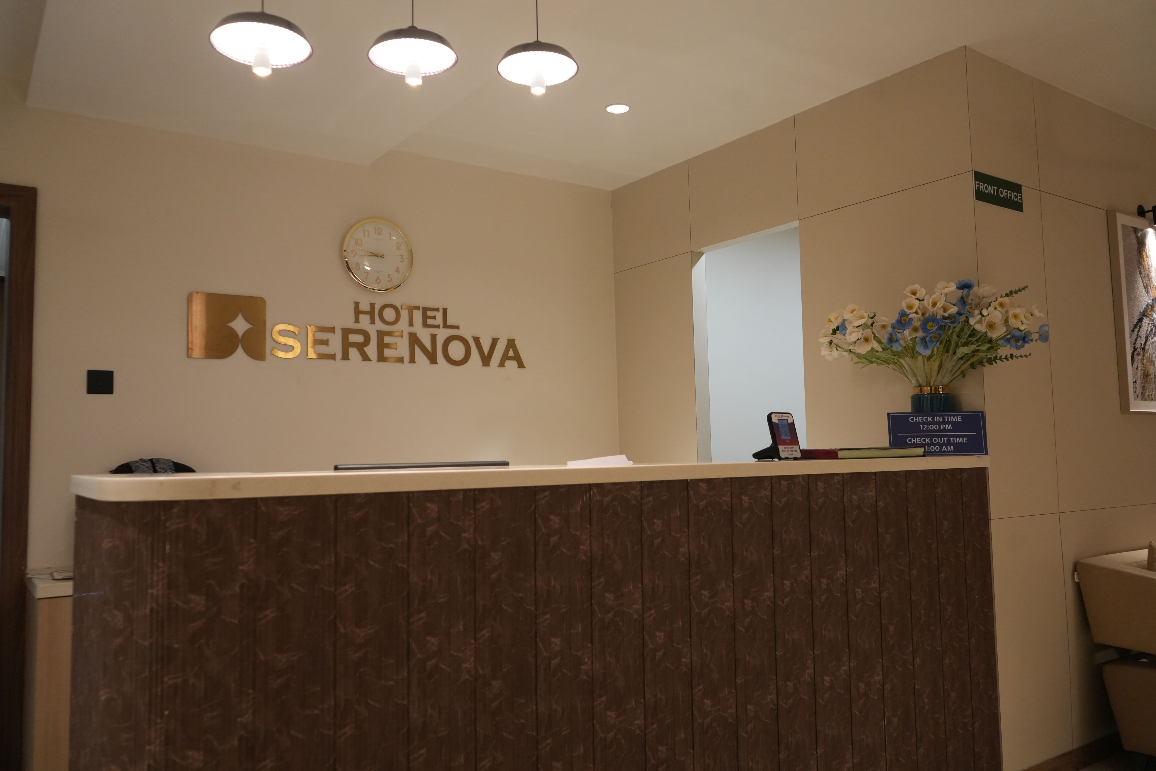 Una recepción de hotel con un reloj, un letrero de la oficina principal y un jarrón de flores.
