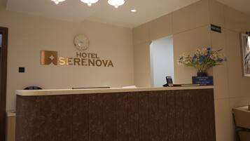 Una recepción de hotel con un reloj, un letrero de la oficina principal y un jarrón de flores.
