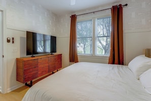 A bedroom with a bed, a TV on a wooden dresser, and a window with curtains. - 5 Mi to UF! Luxury 2-Unit Combo w/ Hot Tub (Gainesville)