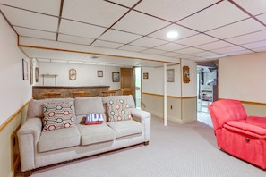 Een woonkamer met een beige bank, een rode fauteuil en een kussen met een patroon.