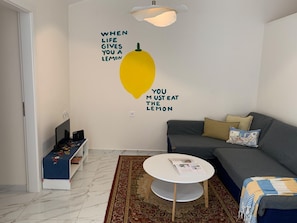 Ein modernes Wohnzimmer mit einer Couch, einem Couchtisch, einem Bücherregal und einer Wand mit einer Zitronenillustration und einem motivierenden Zitat.