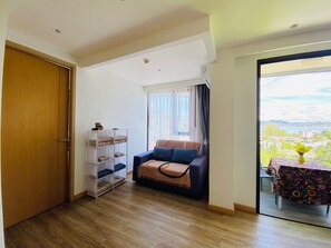 Ein Zimmer mit Holztür, einer Couch mit Kissen, einem weißen Regal und Blick durch eine Glastür.