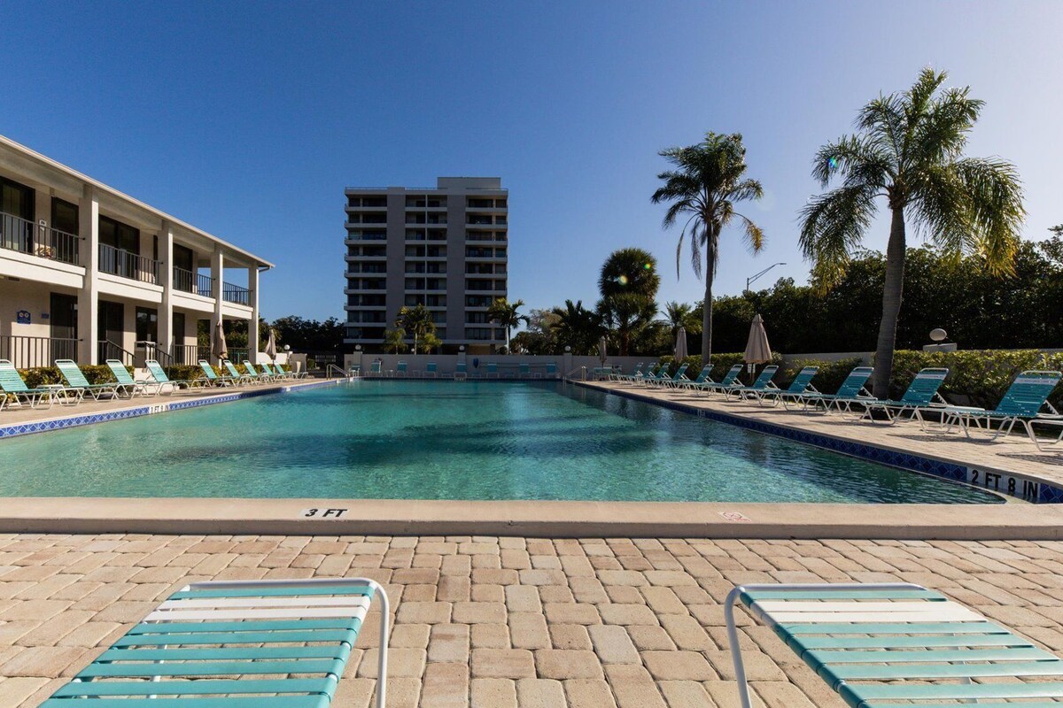 A pool area with lounge chairs and a building in the background.