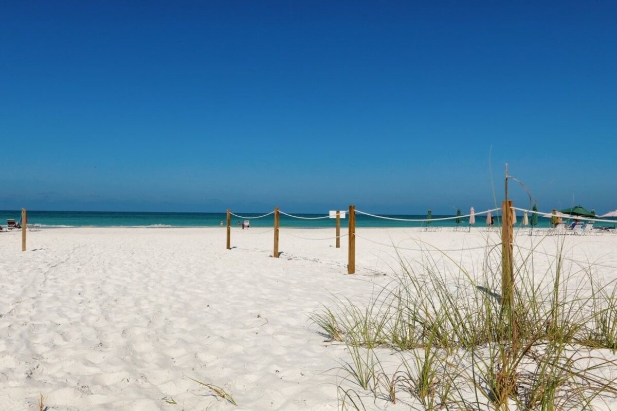 A beach with a rope barrier, a colorful umbrella, and a clear blue sky.