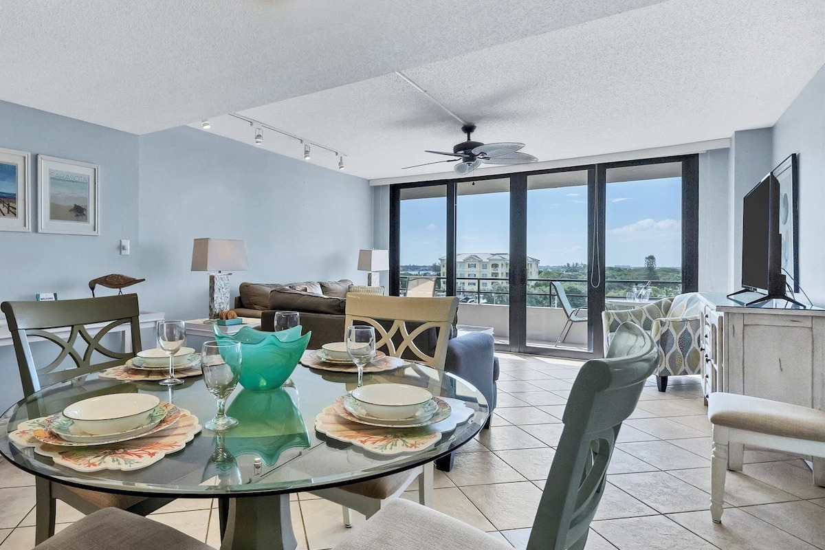 A modern dining area with a glass table, chairs, and a view of the city.