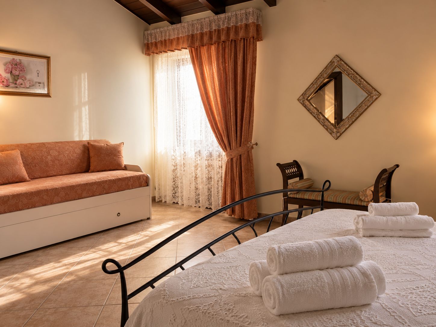 Une chambre avec un canapé, un lit avec des serviettes pliées, une chaise, un miroir et une fenêtre avec des rideaux.