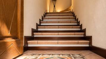 A staircase with wooden steps and a patterned floor, leading to a room with a door and a wall-mounted light fixture.