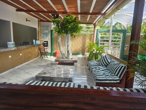A covered outdoor seating area with a sofa and chairs, a wooden floor, and a central tree. - GalyRod House Hotel (San Andrés)