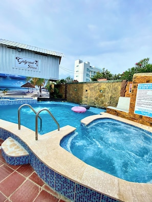 A hotel pool area with a hot tub, lounge chairs, and a sign indicating pool usage rules. - GalyRod House Hotel (San Andrés)