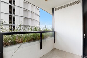 Ein Balkon mit Glasgeländer, einer weißen Wand und Blick auf ein Gebäude mit vielen Fenstern.