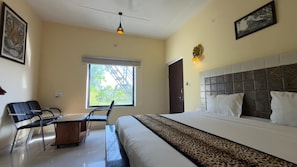 Una habitación de hotel con una cama, un escritorio, una silla, un ventanal y obras de arte en las paredes.