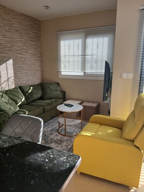 A living room with a sofa, a yellow armchair, a coffee table, and a television. - Cielo Dorado – Luxury Ibiza-Style Apartment with Sunny Rooftop (Alhama de Murcia)