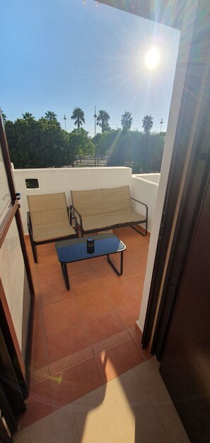 A balcony with a sofa and a table, a clear view of the sky, and a distant view of trees. - Cielo Dorado – Luxury Ibiza-Style Apartment with Sunny Rooftop (Alhama de Murcia)