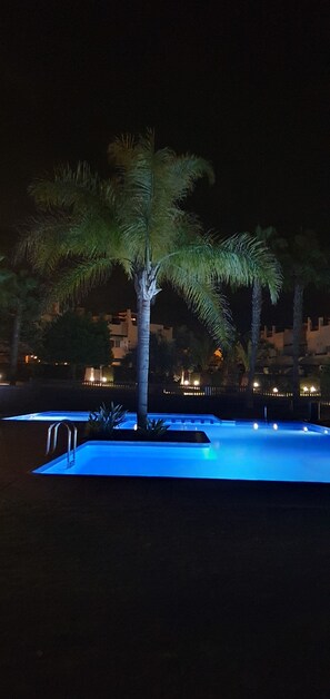 A swimming pool at night with palm trees and a building in the background. - Cielo Dorado – Luxury Ibiza-Style Apartment with Sunny Rooftop (Alhama de Murcia)