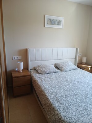 Een slaapkamer met een bed, nachtkastje, lamp, stopcontact en een ingelijste foto.