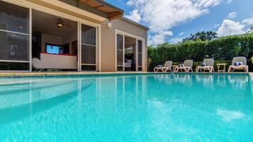 A swimming pool with a clear blue water surface, adjacent to a building with a sliding glass door leading to a bedroom.