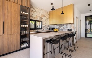 A modern kitchen with a central island, bar stools, a stone backsplash, and wooden cabinetry. - Cozy home in Kastel Stari with private swimming pool, can be inside or outside (Kastel Stari)