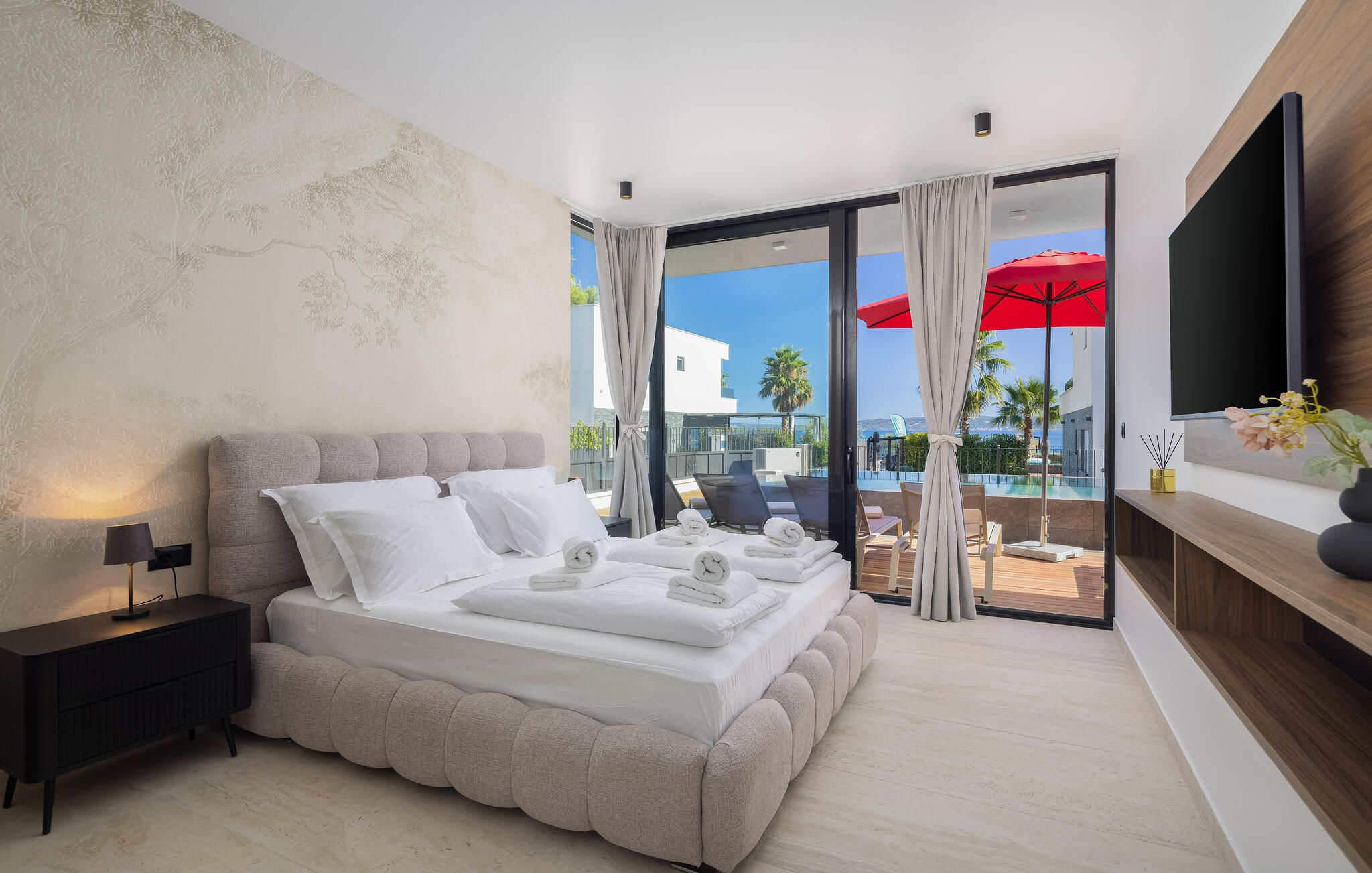 Habitación de hotel moderna con una cama grande, un televisor de pantalla plana, un balcón con vista a la piscina y un comedor.