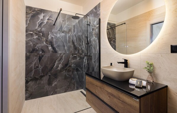 A modern bathroom with a marble shower wall, a round mirror, and a wooden vanity with a sink. - Cozy home in Kastel Stari with private swimming pool, can be inside or outside (Kastel Stari)