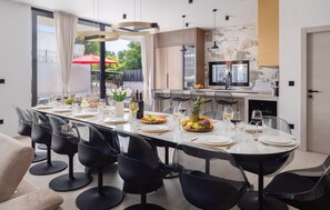A modern dining area with a long table, multiple chairs, and a kitchen in the background. - Cozy home in Kastel Stari with private swimming pool, can be inside or outside (Kastel Stari)