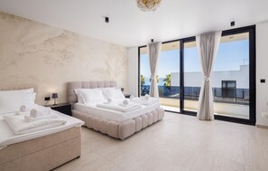 Quarto de hotel moderno com duas camas, uma janela grande e vista para o mar, e uma varanda.