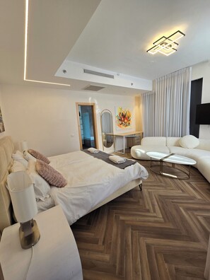 A modern hotel room with a large bed, a white sofa, a small table, and a mirror. - JTower Royal Suites & Penthouse (Jerusalem)