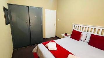 Une chambre d’hôtel avec un lit, une armoire, une table de chevet et une porte.