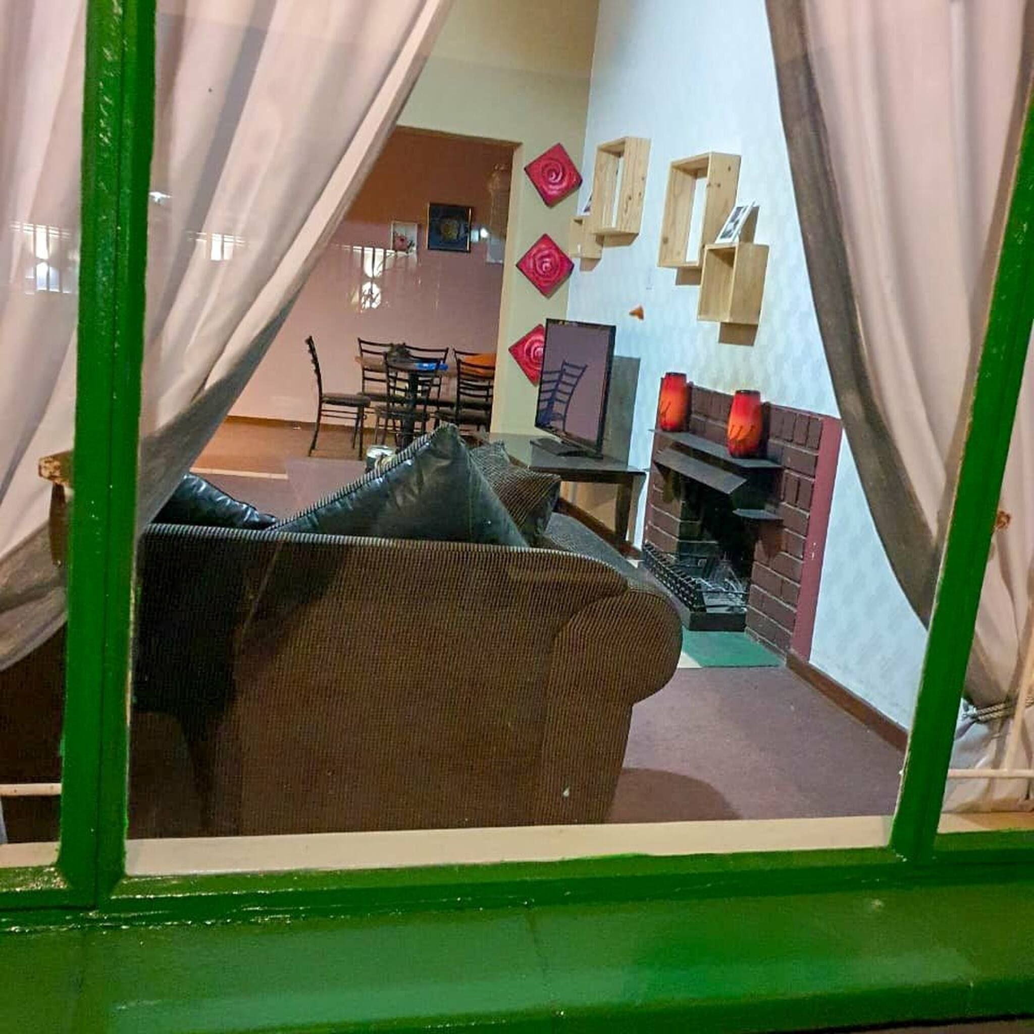 Une pièce avec une fenêtre à cadre vert, un canapé marron, une table à manger avec des chaises et une cheminée décorée de lanternes rouges.