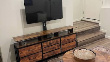 A modern living room with a flat-screen TV mounted on a wooden cabinet, a round coffee table with a bowl, and a patterned rug.
