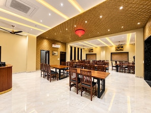 A conference room with multiple tables and chairs, a ceiling fan, and a red chandelier. - Hotel BM Residency (Phalodi)