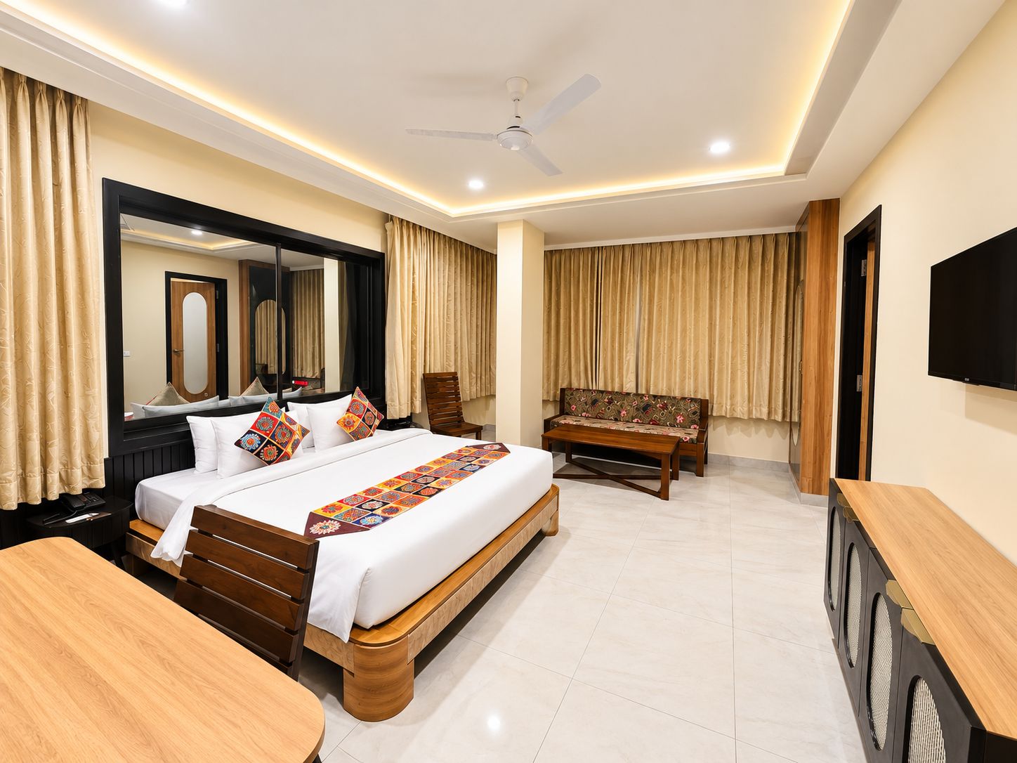 Habitación de hotel con cama, escritorio, silla, sofá, televisor y ventilador de techo.