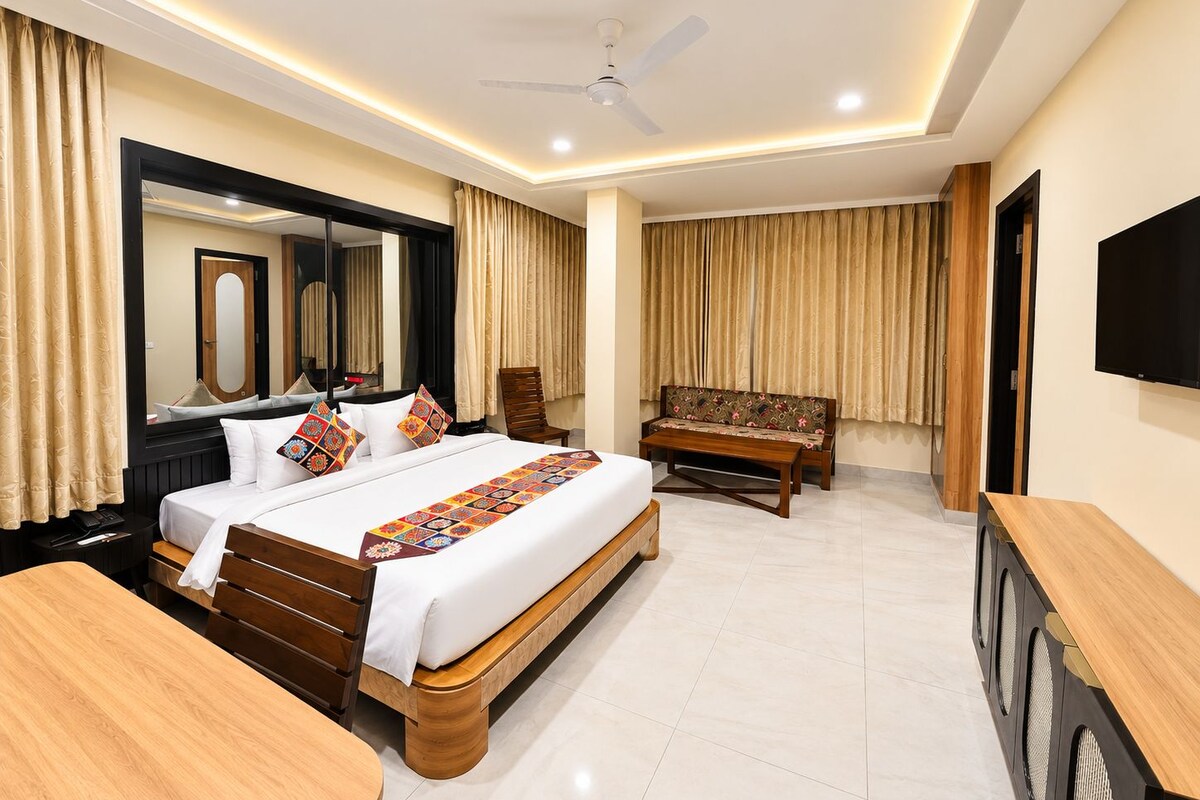 Habitación de hotel con cama, escritorio, silla, sofá, televisor y ventilador de techo.